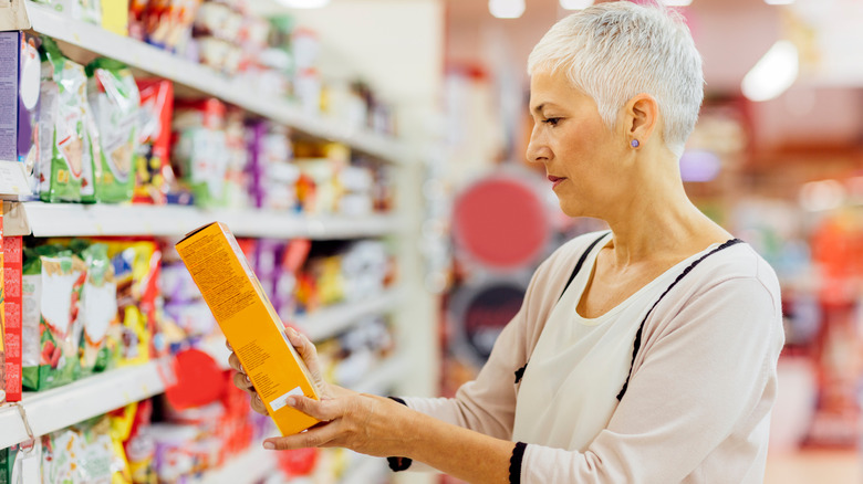Grey-haired woman considering boxed product at grocery store