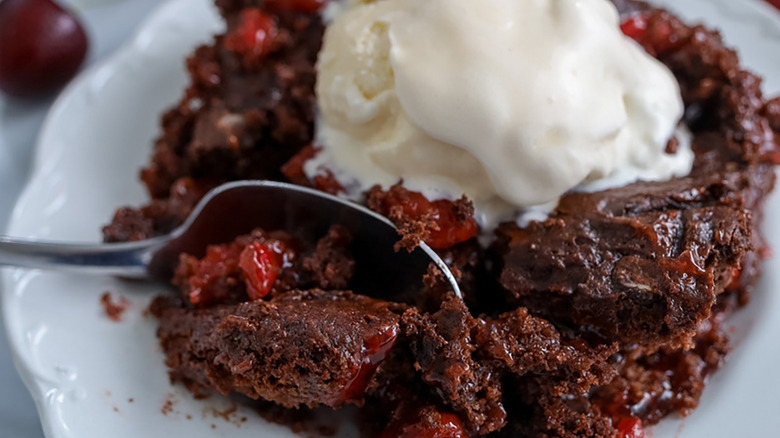Portion of chocolate cherry dump cake on plate, topped with vanilla ice cream
