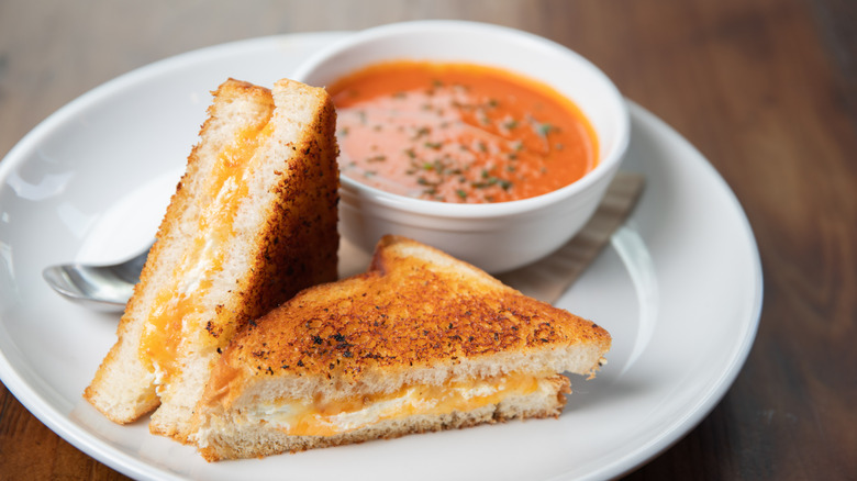 Halved grilled cheese sandwich on white plate with bowl of tomato soup