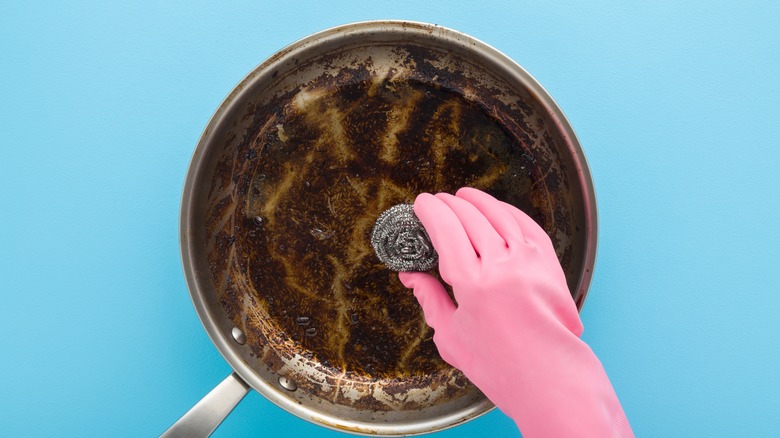 Person cleaning frying pan with steel wool