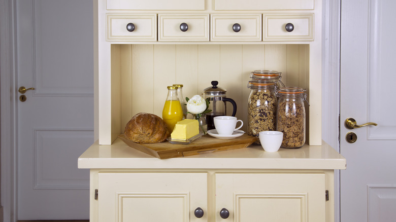 White kitchen hutch filled with cereals in Kilner jars, cups, butter and a French press