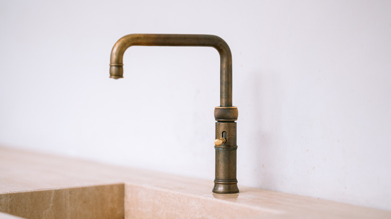 A brass faucet above a deep marble sink with a white backsplash