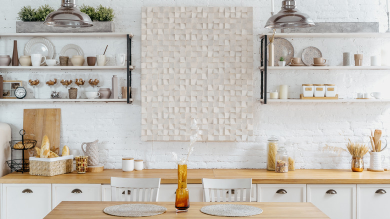 A rustic white kitchen with deep open shelves displaying a collection of cups, glasses, and plates