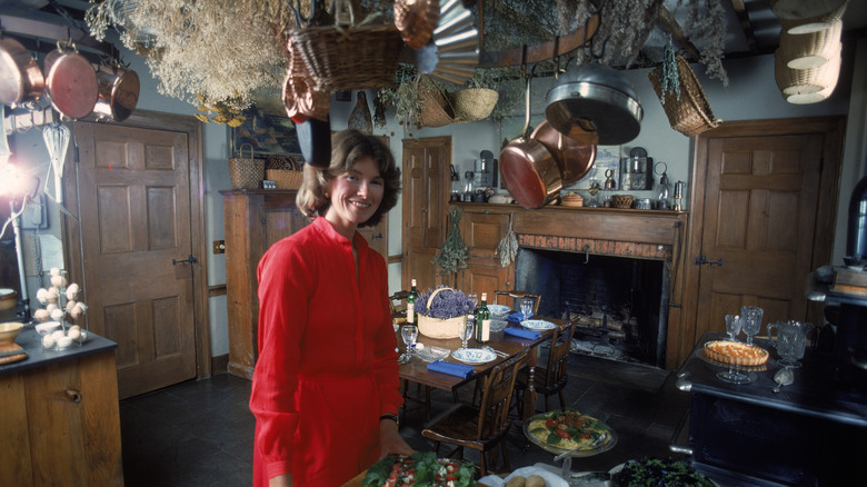 Martha Stewart standing in a red dress in her kitchen with copper pots and baskets on overhead racks