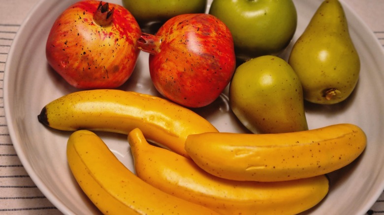 Close-up of bowl filled with artificial fruits, including bananas, pomegranates and pears