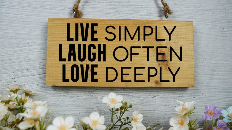 Wooden sign with motivational text hanging against a grey wall with A