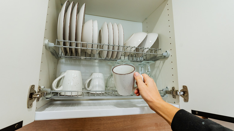 Hand placing mug inside kitchen cupboard