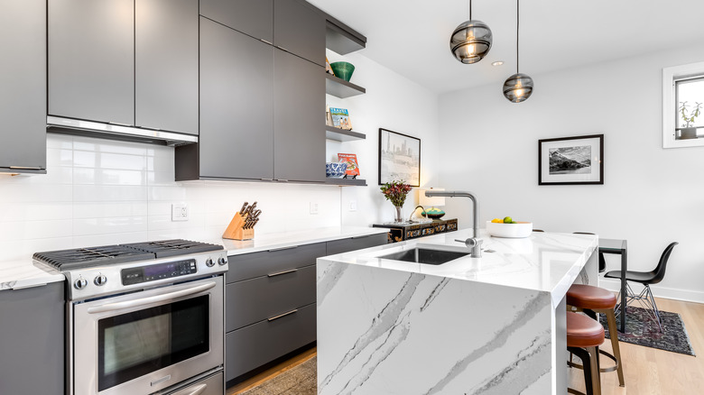 Modern kitchen with grey cabinets, white marble waterfall island and overhead pendant lights