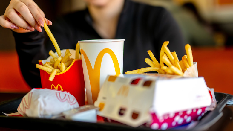 Person taking a fry out of a container on a tray with burgers and a drink at McDonald's