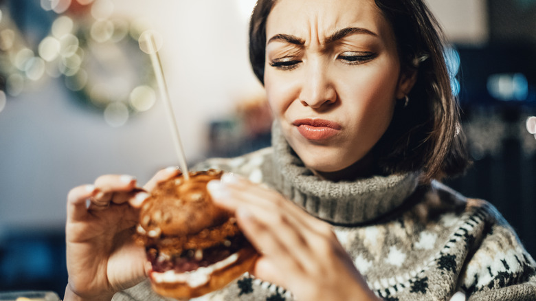 Woman in a sweater scowling at a burger
