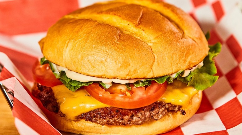 Smashburger with cheese and tomato on red and white paper