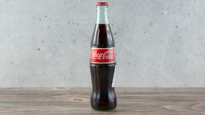 Bottle of Mexican Coca-Cola on a wooden table in front of a cement wall
