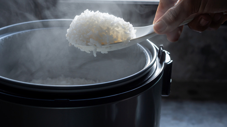A hand scooping steaming hot white rice out of a rice cooker