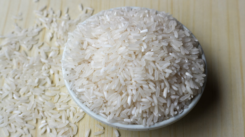 Raw rice in white bowl on wooden background