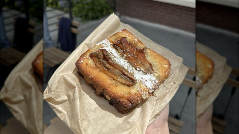 Hand holding bostock topped with sliced banana and powdered sugar