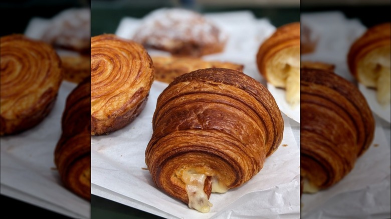 A ham and cheese croissant alongside other pastries on paper