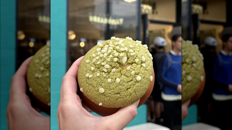 A hand holding a kaya bun outside a shop