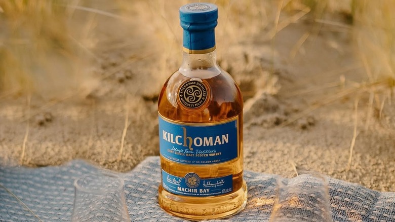 A bottle of Kilchoman Machir Bay placed on a blanket on a sandy beach