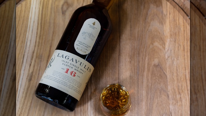 A bottle of Lagavulin 16 on top of a whisky barrel with a filled glass