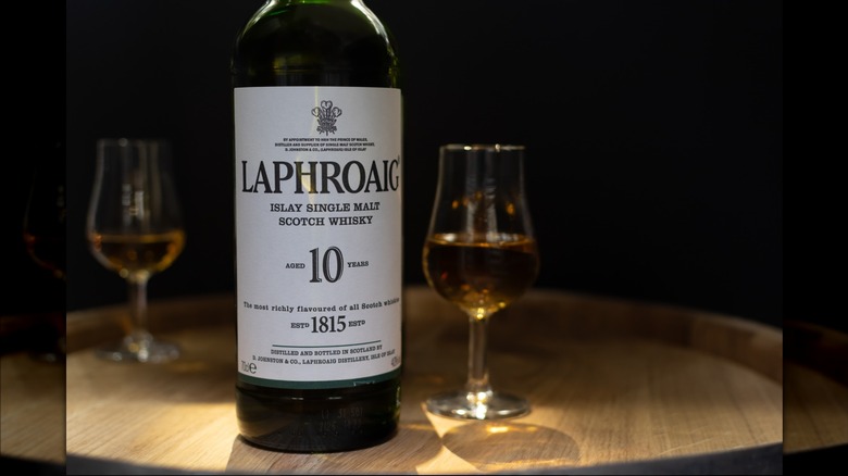A bottle of Laphroaig 10 on top of a whisky barrel with two filled glasses either side