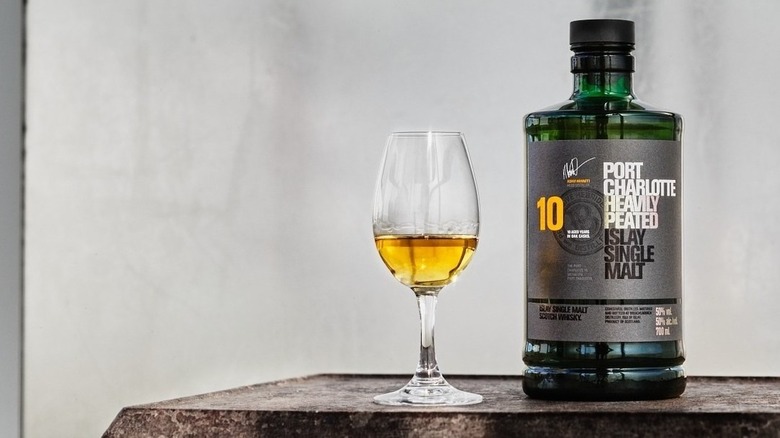 A bottle of Port Charlotte 10-year perched next to a full glass against a plain background