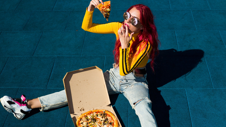 Girl sitting on the ground outside with a slice of pizza and pizza in box