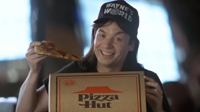 Still from Wayne's World of Wayne holding slice of pizza and Pizza Hut box