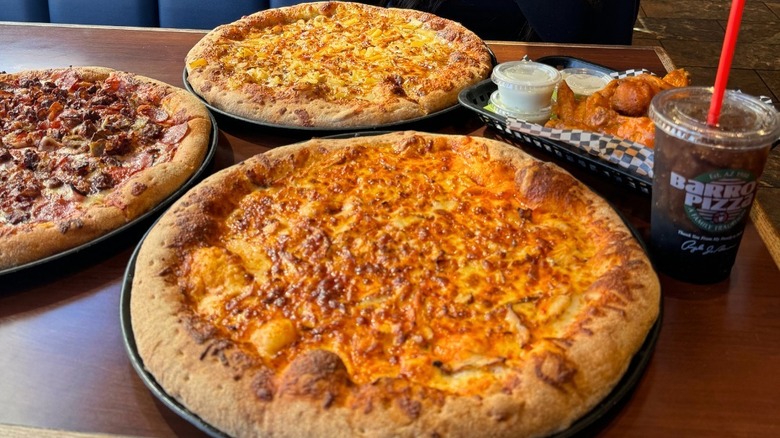 Three Barro's Pizzas on a restaurant table next to a basket of wings and a soda