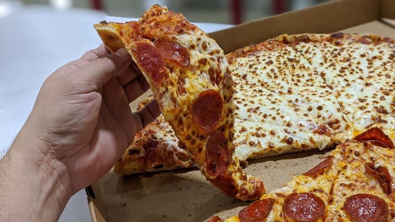 A hand grabbing a slice of pepperoni pizza from a box of Costco pizza at the food court