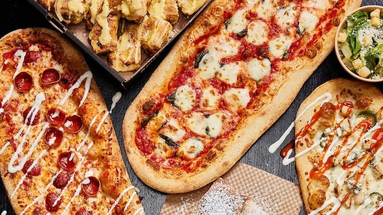 Oblong pizzas from &pizza on a table with a side salad and bread
