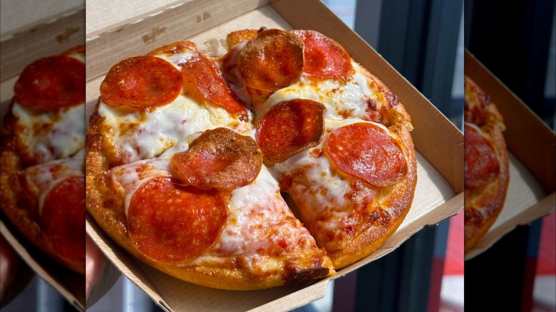 A person holding a small box containing a pepperoni Pizza Hut Personal Pan Pizza