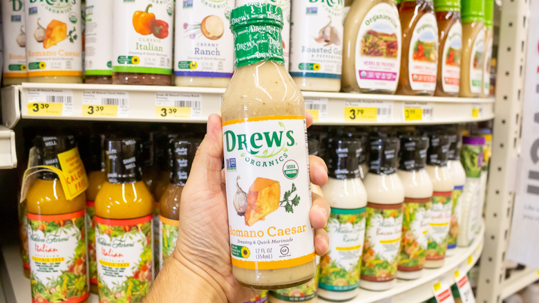 A view of a hand holding a bottle of Drew's Organics Romano Caesar salad dressing at a grocery store