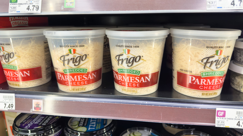 A view of several containers of Frigo shredded parmesan cheese on display at a grocery store.