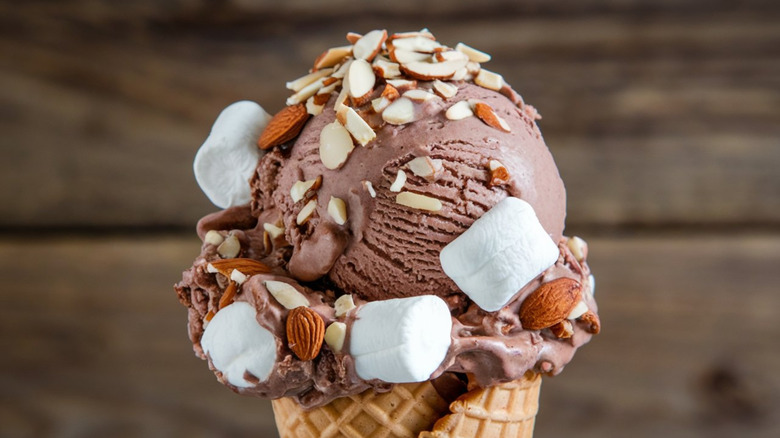 Close-up image of a scoop of rocky road ice cream in cone against a dark brown background