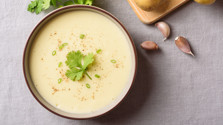 Top view of a bowl of creamy potato soup garnished with fresh parsley with garlic cloves on the side