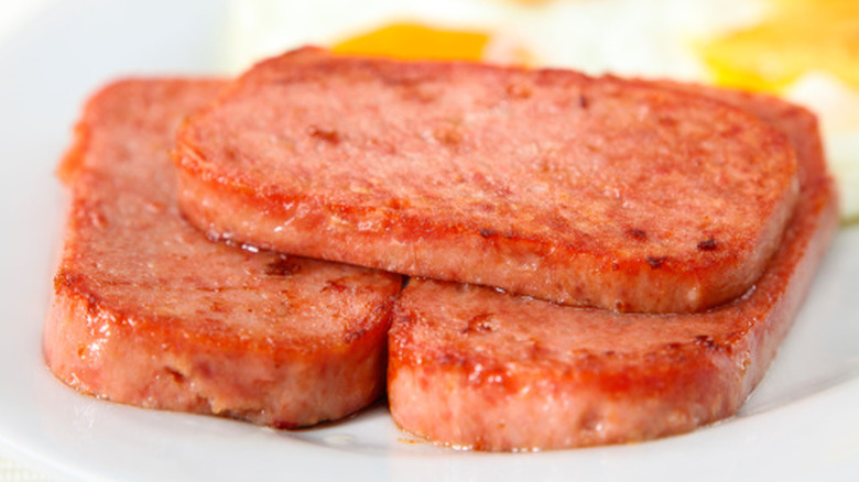 Fried Spam slices on plate with fried eggs in background