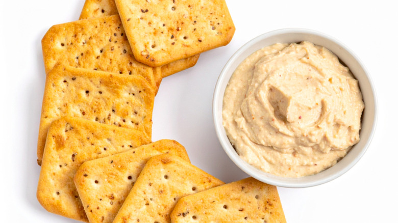 Crackers and bowl of hummus on white background