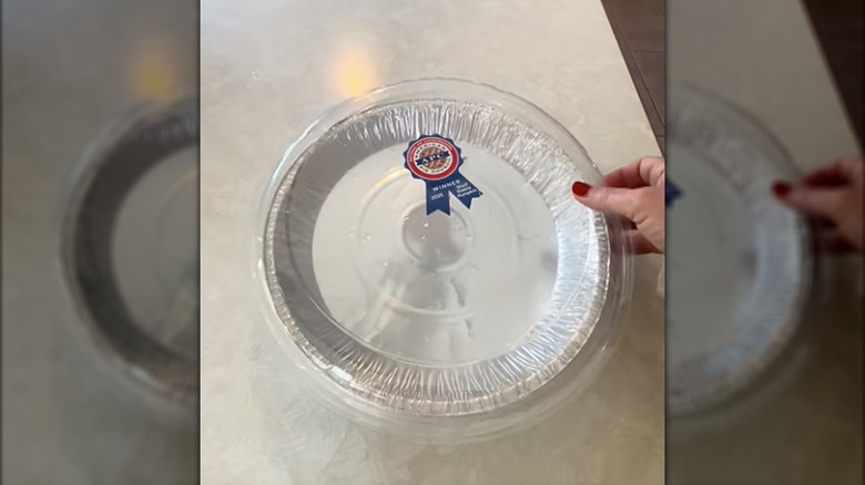 Hand holding empty pie plate with plastic covering