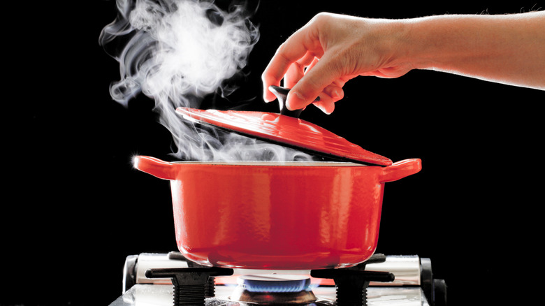 Hand lifting the lid of hot Dutch oven on stove with plume of steam