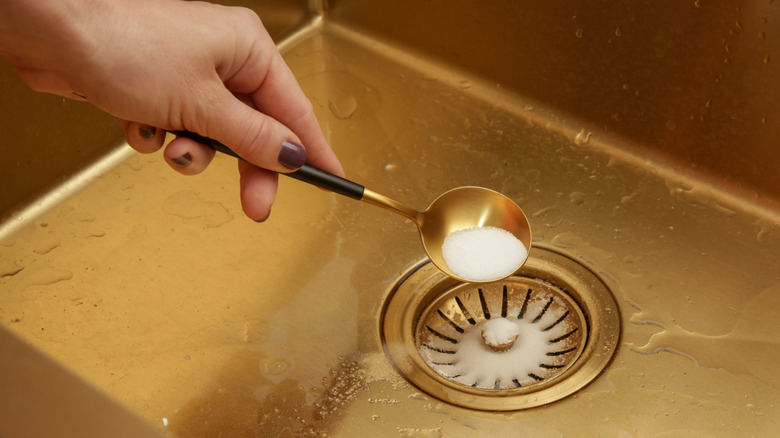 Hand holding a spoon of baking soda above a kitchen sink