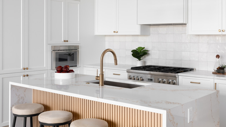 White kitchen with a waterfall island and golden faucet on the sink