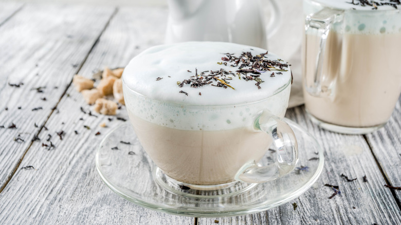 London Fog latte in a small glass cup sprinkled with tea leaves with another drink in the back