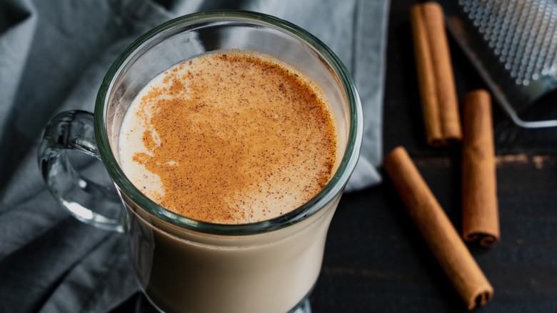 Cozy rooibos latte with pumpkin spice in a glass mug with cinnamon sticks on the side