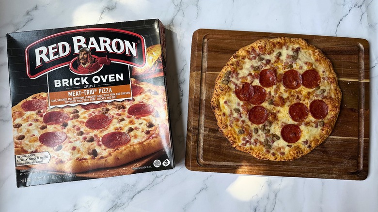 Red Baron Brick Oven Meat Trio pizza box next to pizza on cutting board