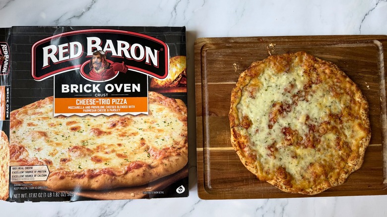 Red Baron Brick Oven Cheese Trio pizza box next to pizza on cutting board
