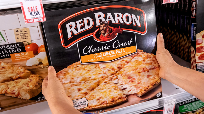 Two hands holding box of Red Baron four cheese pizza