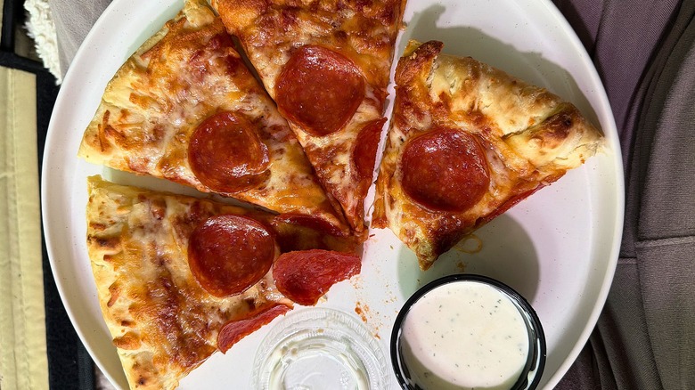 Top-down shot of four slices of pepperoni pizza on white plate next to small cup of ranch dressing