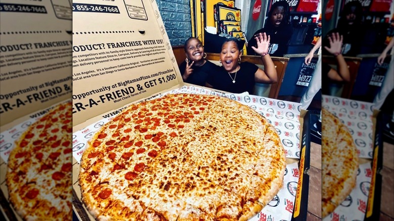 Two girls in front of a gigantic pizza in a box from Big Mama's & Papa's