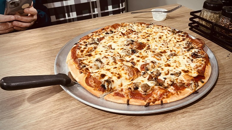 Pizza on a silver plate with pizza slice underneath in the middle of restaurant table