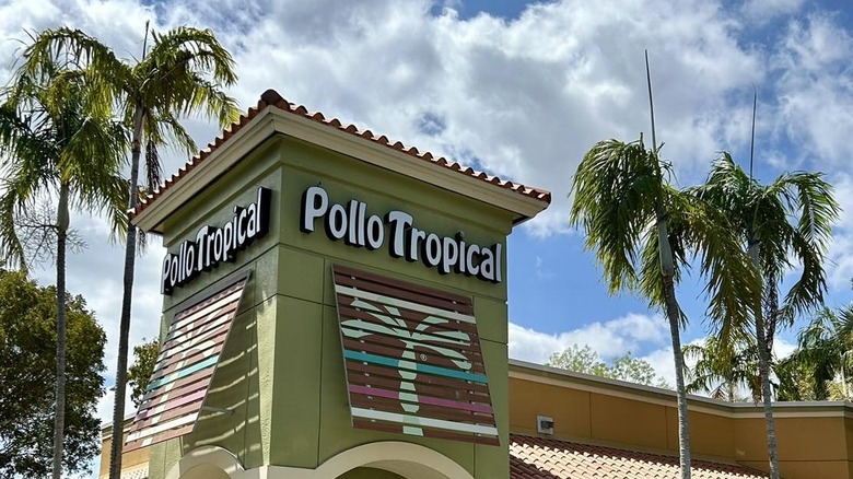 Exterior of Pollo Tropical restaurant with palm trees on both sides